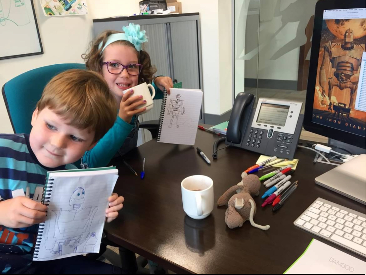 Two of the author's children sitting at a desk with notebooks and pens, busy drawing at work in the studio